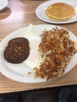 Eggs over easy, two pancakes, sausage patties and well done hash browns