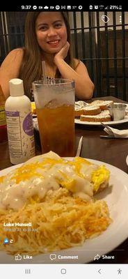 Scrambled eggs topped with gravy and cheese served with hash browns and in the background French toast topped with powdered sugar