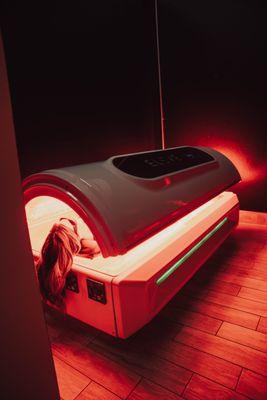 Client in a full-body red light bed, enhancing skin health, reducing inflammation, and supporting muscle recovery and relaxation.