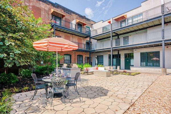 An outdoor courtyard with a chair and an umbrella surrounded by apartments at Wireworks Lofts in the Square.