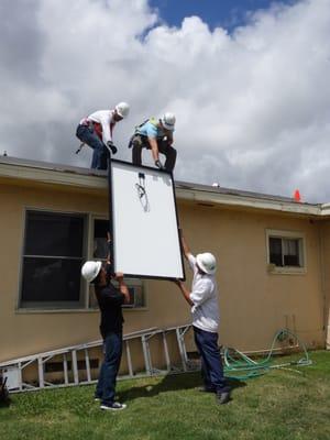 Volunteers pass a solar panel up onto the roof.