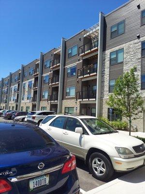 Apartment balconies overlooking spacious, well-maintained parking lot with tree tops in the distance.