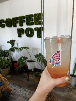 Sunset Lotus drink in front of The Coffee Pot's indoor swing and signage.