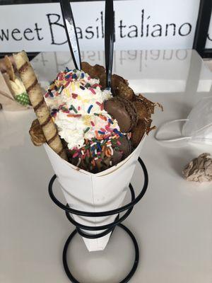 Bubble waffle cone with peanut butter ice cream, peanut butter drizzle, chocolate macaroon, chocolate stick, whipped cream and sprinkles