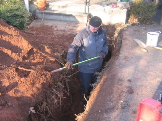 Bob digging up a water main, the last part has to be done by hand because of the risk of a machine breaking the pipe.