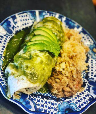 Pastor burrito topped with tomatillo sauce with a side of rice and beans.