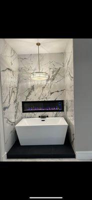 New stand along bathtub. With tiled surrounding and electric fireplace.