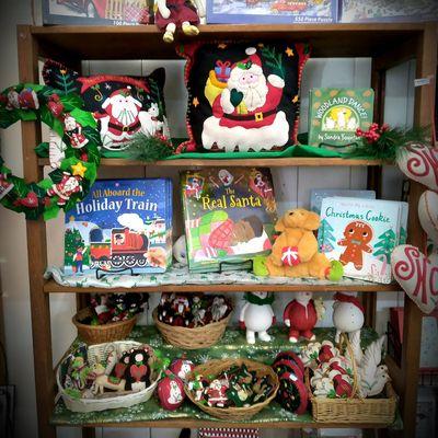 Holiday pillows and ornaments on display among some Christmas books on the shelf.