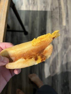 Sausage and cheese kolache with some hardened crusty cheese on outside.