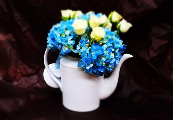 Flowers, Naturally! - blue hydrangeas and white spray roses in a customer-supplied milky-white teapot. A custom floral mini-composition.