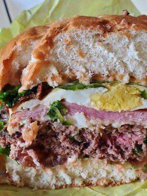 The layers of a X-Tudo. Bread, sauce, patty, tomato, cheese, ham, egg, bacon, lettuce...