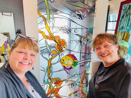 Penny and Brandy in front of one of a pair of underwater fish art glass overlay panels they worked on!