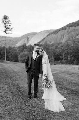 Man in a three piece suit, woman in a white wedding gown, in front of a mountain