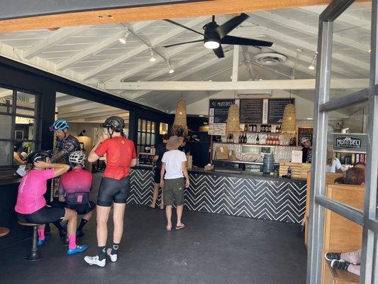 Some cyclists are lining up for grub. Next door is a cycle shop.