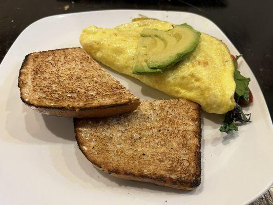 Cheese omelette with avocado, tomato, and greens. Toast on the side.