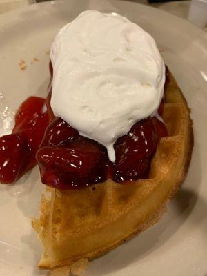 Half a Belgian waffle with strawberry and whip cream