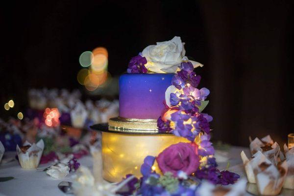 Wedding cake, fresh flowers, lights, decorated as a purple sunset with stars starting to appear.