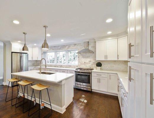 A classic Shaker-style white kitchen with light countertops and warm wood floors exudes timeless elegance and a welcoming ambiance.