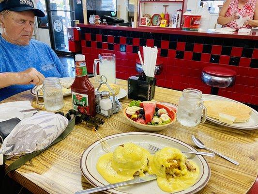 Crab Cakes Benedict, Bowl of Fresh Fruit, a giant Hot Cake and Ray's Country Fried Steak & Eggs is behind the mug.