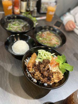 On left broth & side of jasmine rice, on right steak phó, in front grilled pork & egg roll vermicelli