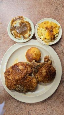 Two pork chop dinner with mac and cheese, mashed potatoes and gravy, and a corn roll.