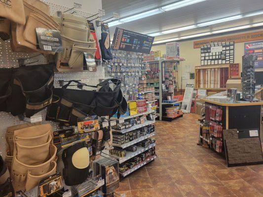 A Builders FirstSource store interior showing a display of tool belts, knee pads, and various building supplies organized on ...