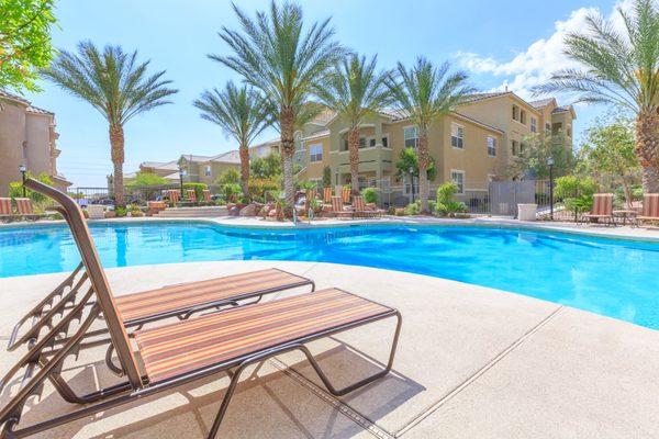 Poolside lounge seating next to resort-style pool and mission-inspired property exterior.