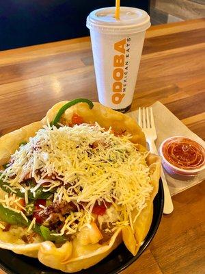 Brisket burrito in a taco shell bowl, with a drink and a side of salsa roja.