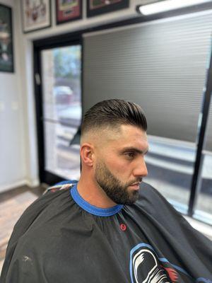 Mid high skin fade with a slick back and a blended beard line up