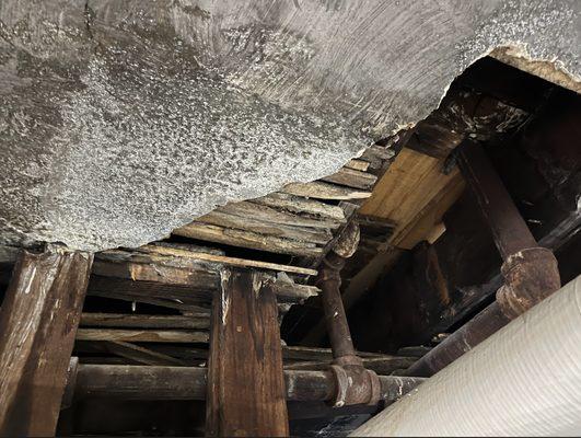 One of many gaps in the ceiling with water damage and exposed wood beams