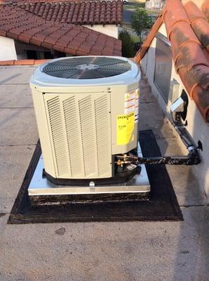 Residential flat roof AC installation with electrical and refrigerant routing.