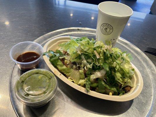 Chicken burrito bowl with a side of guac, chipotle Tabasco sauce, and a cup of water.