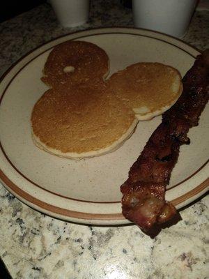 Mickey Mouse pancake with slice of bacon.