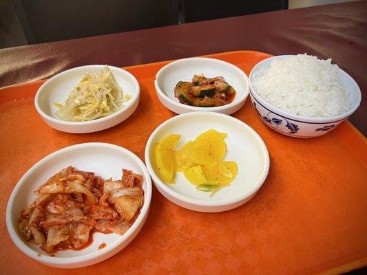 Top left to right: bean sprouts, spicy cucumbers, steamed white rice.  Bottom left to right: kimchi, yellow radish