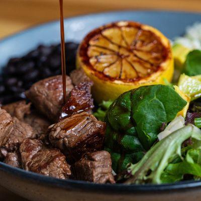 TENDERLOIN BOWL: Featuring juicy tenderloin, cilantro lime rice, slow-cooked black beans, fresh avocado, and spring mix, all topped with a s