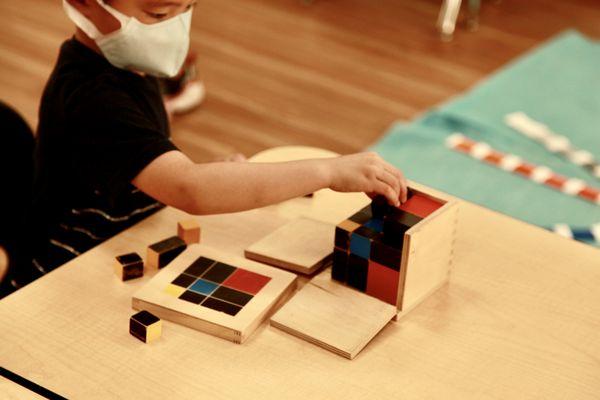 A child is working with  Montessori trinomial cube.