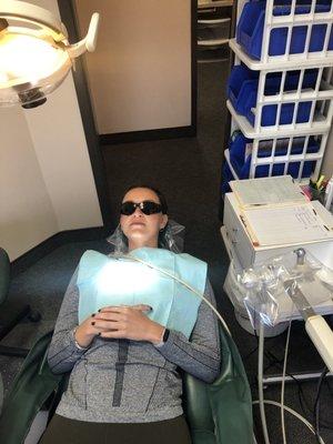 A woman getting her teeth cleaned. Sunglasses provided by the office.