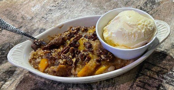 Homemade peach cobber topped with Candied Pecan served with a side of vanilla ice cream.