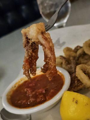 A piece of the Calamari being pulled out of the Marinara sauce with a fork.