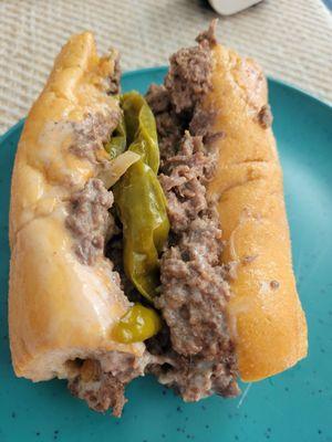 Half of a small cheesesteak with long hots.