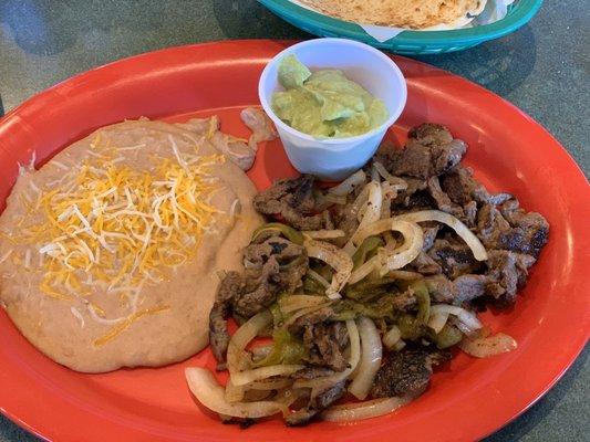 Beef fajitas with beans, guacamole, a green chile strip and sautéed onions.