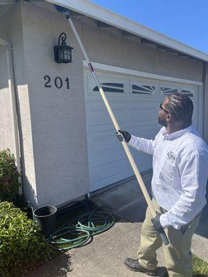 Pest control technician removing all the current spider webs underneath the eaves of the garage