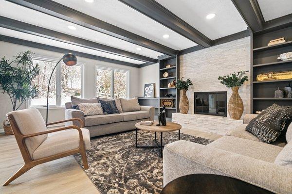 modern living room with fireplace, recessed lighting, exposed beams painted black, built-in bookshelves, casement windows, couches and chair