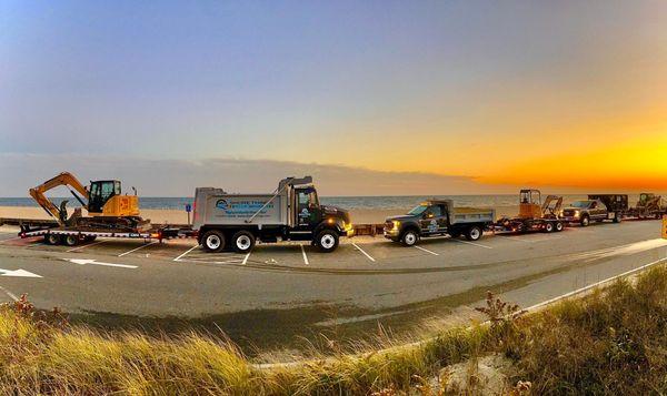 Shore Things Environmental fleet of trucks at a beach parked in parking lot with ocean in background and sun setting