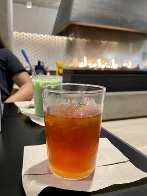 Iced black tea with honey, and an iced matcha latte with vanilla. both are in glasses with a fireplace in the background!