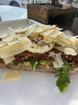 Architectural Toast -Seeded Bread  Smashed avocado, our house arugula salad, bacon, fried egg, everything seasoning, shaved parmesan.