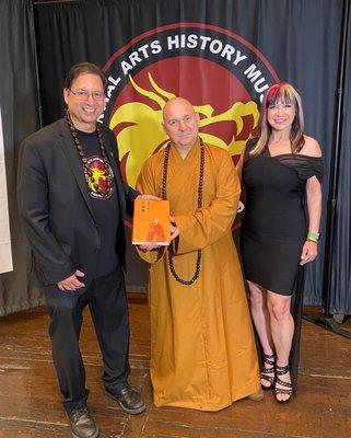 Venerable Shi Yanfan offering Venerable Abbot Shi Yongxin's book to Michael Matsuda with Cynthia Rothrock