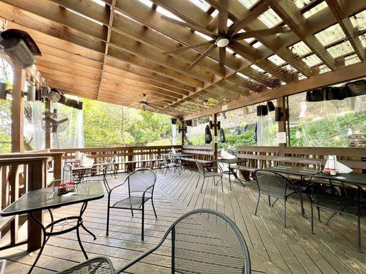 Outdoor shaded patio with fans and space heaters overhead.