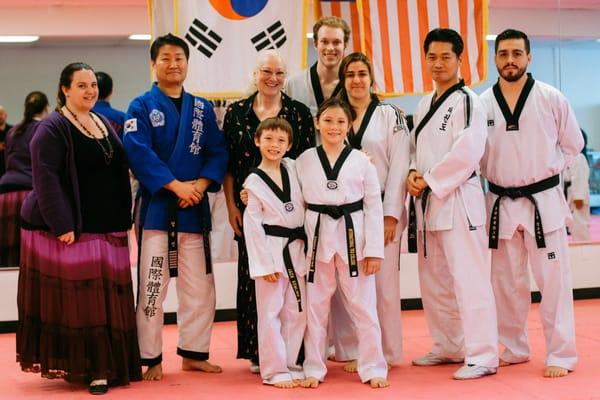 After black belt testing, two students pose with the testing instructors, studio instructors, and studio owner Master Park.