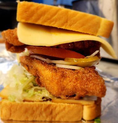 This is a catfish sandwich with smoky & savory cheese, lettuce, pickles, onions, and a tomato.